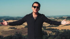 Christian Nodal está de pie con los brazos abiertos de par en par y las palmas hacia arriba, sonriendo ligeramente.