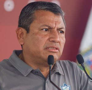 Hombre de avanzada edad y rostro reacio hablando ante un micrófono.