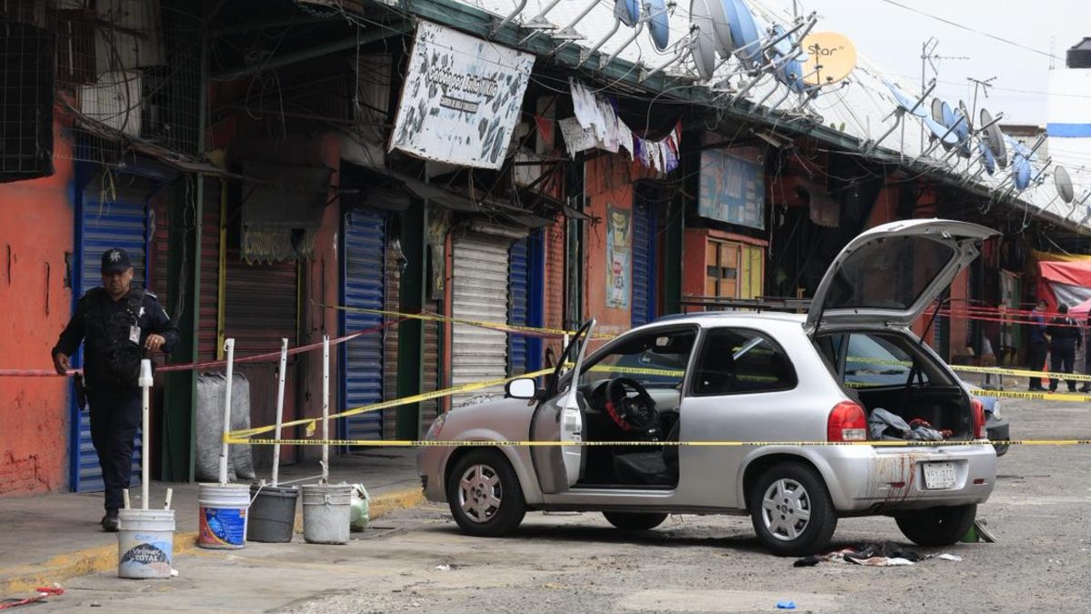 Policía camina junto a un auto acordonado con cintas de seguridad en el Mercado Morelos de Puebla.