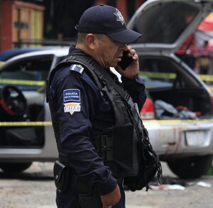 Policía hablando por teléfono junto a un vehículo asegurado.