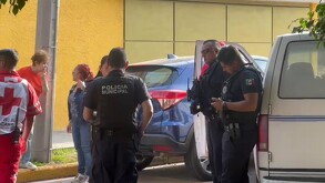 Tres policías de Guadalajara hablando con una mujer con un paramédico de la Cruz Roja a un lado, dos mujeres al fondo y dos camionetas alrededor