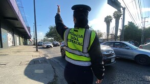 Vista de espaldas de una agente de la Policía Vial Estatal de Jalisco levantando la mano para dar paso a los autos que circulan en la calle
