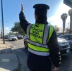 Vista de espaldas de una agente de la Policía Vial Estatal de Jalisco levantando la mano para dar paso a los autos que circulan en la calle