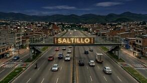 Se observa un punete peatonal, varios carros transitando por la vialidad; es de noche y hay letras que dicen Saltillo.