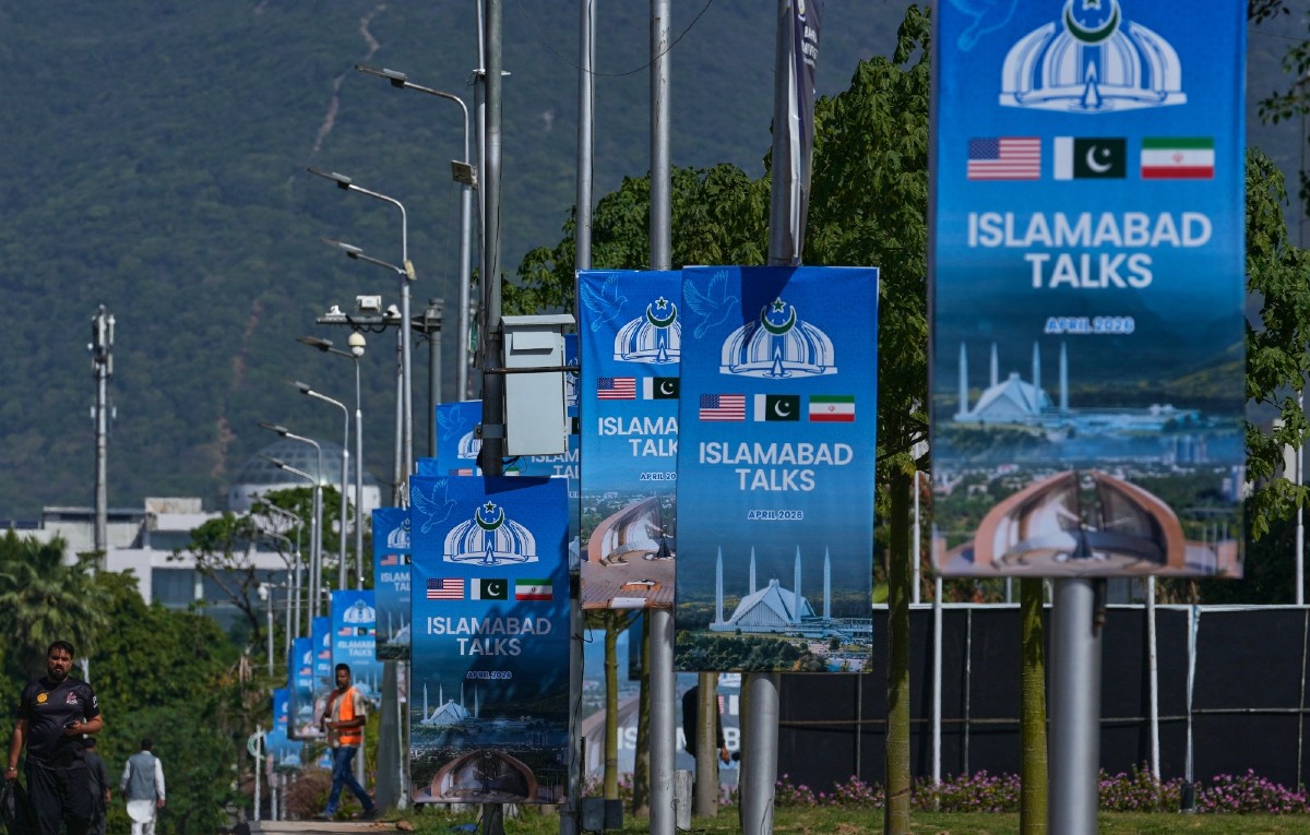 Trabajadores pasan junto a vallas publicitarias cerca del Hotel Serena antes de la segunda ronda de negociaciones entre EEUU e Irán, en Islamabad, Pakistán.