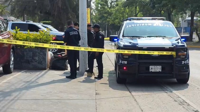 Oficiales de la Policía de Zapopan al lado de una patrulla resguardando un área acordonada con una bolsa donde se encontró un cráneo humano