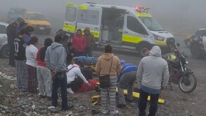 Se observan a varias personas paradas observando al piso, hay una ambulancia y se ve que hay neblina.