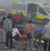 Se observan a varias personas paradas observando al piso, hay una ambulancia y se ve que hay neblina.