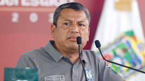 Hombre con una playera policiaca haciendo un gesto mientras habla ante un micrófono.