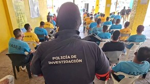 Vista de espaldas de un agente de la Policía de Investigación de Jalisco detrás de un grupo de internos sentados dentro de un centro de rehabilitación