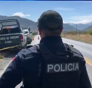 Se observa a un hombre policía de espaldas y una cinta amarilla de precaución.