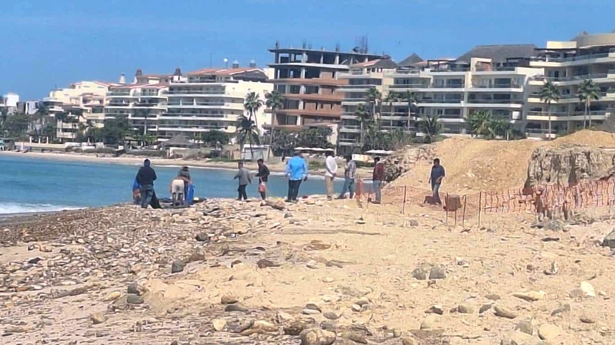 Hombre y trabajadores caminando en Playa Las Cocinas en Punta Mita con un área de construcción cerca de la orilla