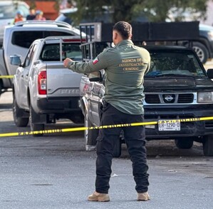 Se observa a un hombre vestido de policía, hay una cintilla amarilla de precaución y hay vehículos estacionados.