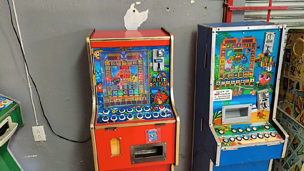 Dos oficiales de la Secretaría de Seguridad de Jalisco vitos de espaldas sosteniendo armas largas con máquinas tragamonedas delante