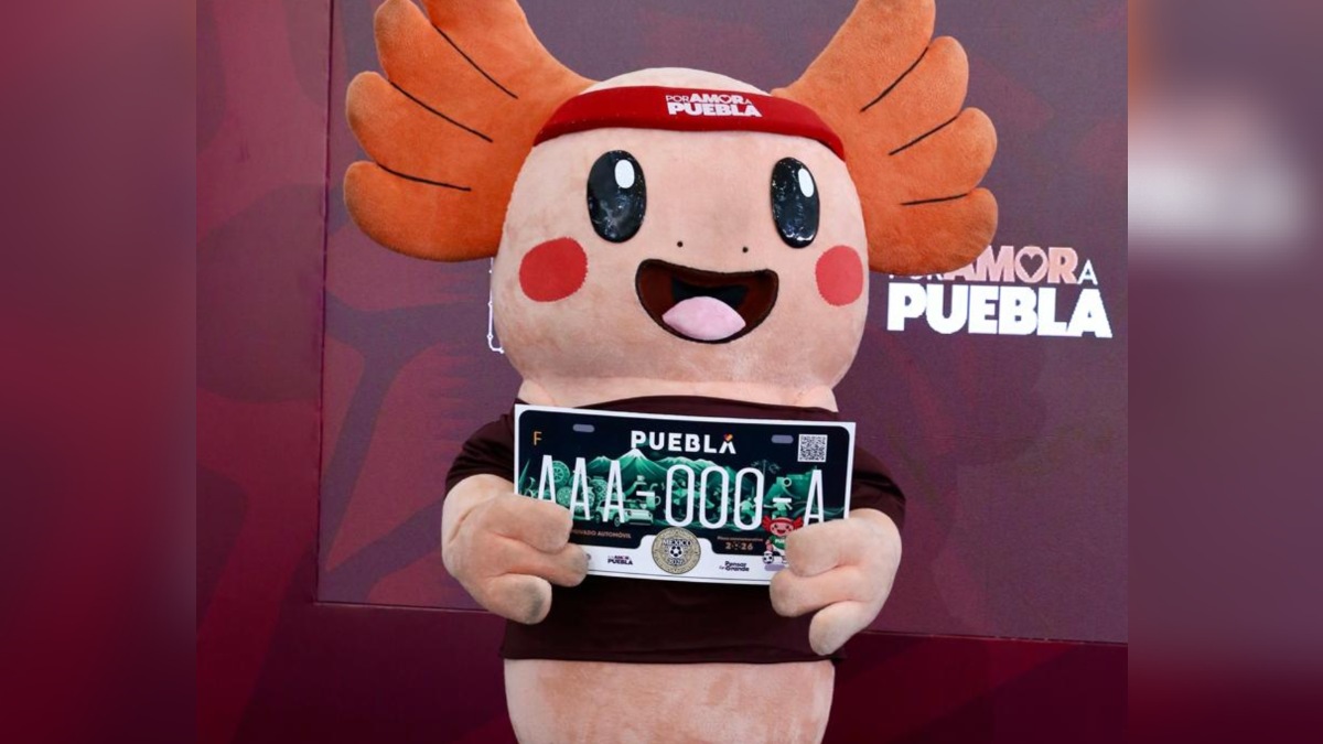 una botarga de ajolote sostiene una placa conmemorativa del mundial 2026 en puebla