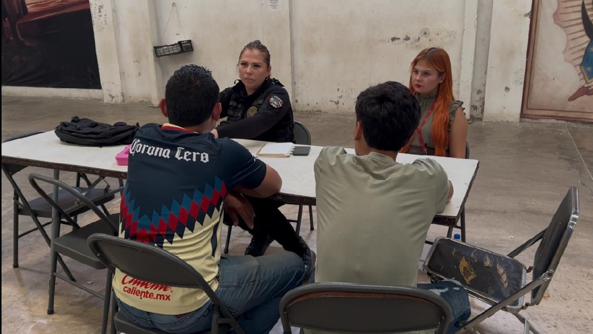 Dos mujeres miembros de autoridades de Tlaquepaque hablando con dos menores de edad vistos de espaldas sentados en una mesa
