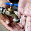 Válvula de agua con dos manos con las palmas extendidas y una cubeta debajo levemente desenfocadas