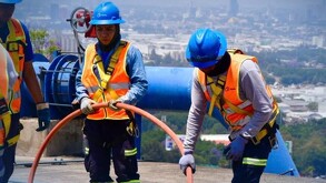 Trabajadores uniformados del Siapa en Guadalajara realizando trabajos en tuberías con una manguera naranja y la ciudad vista en el fondo