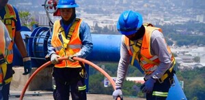 Trabajadores uniformados del Siapa en Guadalajara realizando trabajos en tuberías con una manguera naranja y la ciudad vista en el fondo