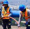 Trabajadores uniformados del Siapa en Guadalajara realizando trabajos en tuberías con una manguera naranja y la ciudad vista en el fondo