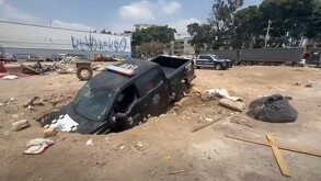 Patrulla de la Policía de Guadalajara con la parte delantera hundida dentro de un socavón en un terreno baldío con basura y escombros alrededor