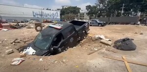 Patrulla de la Policía de Guadalajara con la parte delantera hundida dentro de un socavón en un terreno baldío con basura y escombros alrededor