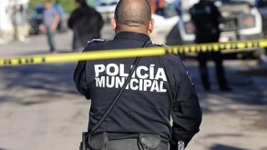 Oficial de la Policía Municipal en Jalisco con una cinta policiaca amarilla acordonando una zona con policías y patrullas desenfocadas en el fondo