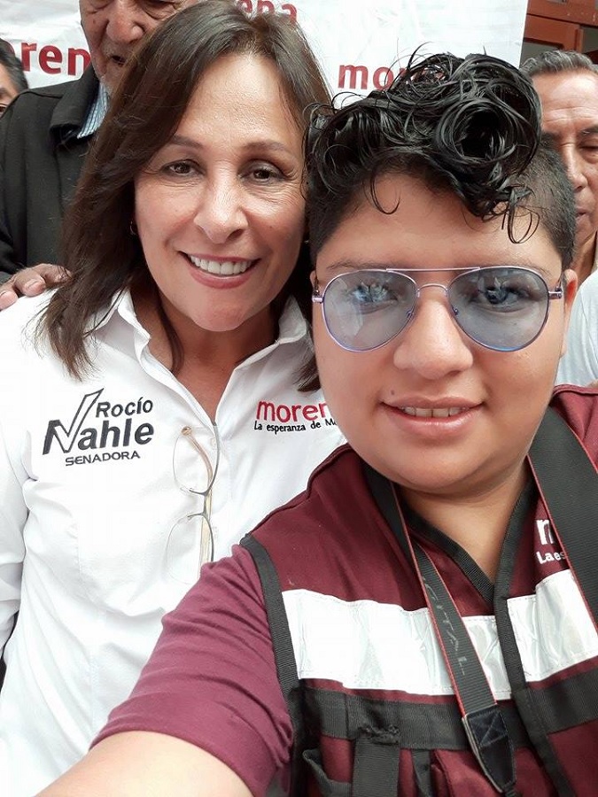Dos mujeres sonriendo para la cámara mientras visten un chaleco guinda con las siglas 