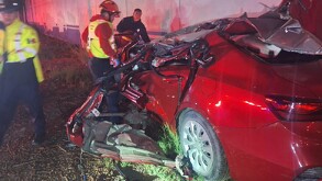 Se observa un vehículo color rojo destrozado, hay un bombero y un policía en el área.