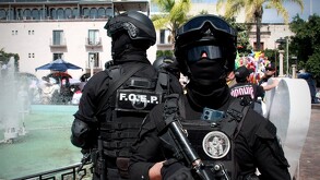 Dos oficiales de las Fuerzas Especiales de la Policía de Jalisco sosteniendo armas largas al lado de una fuente en medio de un parque en Zapopan