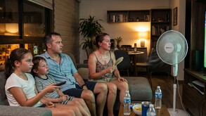 familia viendo la televisión, con mucho calor, mientras un ventilador les da de frente