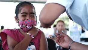 Se observa a una niña con cubrebocas que le están aplicando una vacuna.