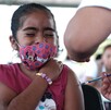 Se observa a una niña con cubrebocas que le están aplicando una vacuna.