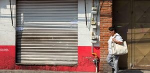 Mujer camina frente a una tienda de la colonia 10 de mayo, en Puebla.