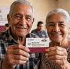 Par de adultos mayores sonriendo a la cámara mientras sostienen su tarjeta de la Pensión Bienestar.