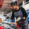 Una mujer en un taller mecánico revisando el nivel de aceite de un auto que tiene el cofre levantado