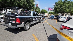 Estacionamiento de Plaza Revolución con autos, moto de policía y una patrulla sosteniendo una cinta policiaca que acordona la escena