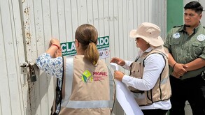 Se observa a una mujer y hombre poniendo un cartelón de clausurado en un portón.