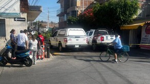 Patrulla de la Policía de El Salto al lado de una camioneta del IJCF detrás de una cinta policiaca con personas y un ciclista viendo la zona