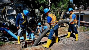 Cuatro trabajadores del Siapa realizando trabajos con una manguera dentro de una tubería en un terreno con maquinaria y plantas