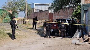 Oficiales de la Policía Municipal de El Salto alrededor de una área acordonada por una cinta policiaca con una patrulla en el sitio