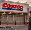 Clientes esperan frente a la entrada cerrada de una tienda Costco con un carrito de compras.