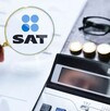 Mano sosteniendo una lupa con el logo del SAT delante de un documento con una calculadora, monedas y unos lentes a un lado