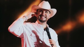 Cantante Eden Muñoz sonriendo mientras sostiene un micrófono durante un concierto con luces de fondo