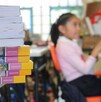 Se observa una niña desenfocada y unos libros; dentro de un salón de clases.
