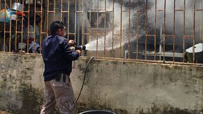 Hombre arroja cubeta con agua a una casa que se incendia.