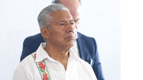 Fotografía del perfil de un hombre anciano vestido con camisa blanca; al fondo, una cabeza de alguien más.