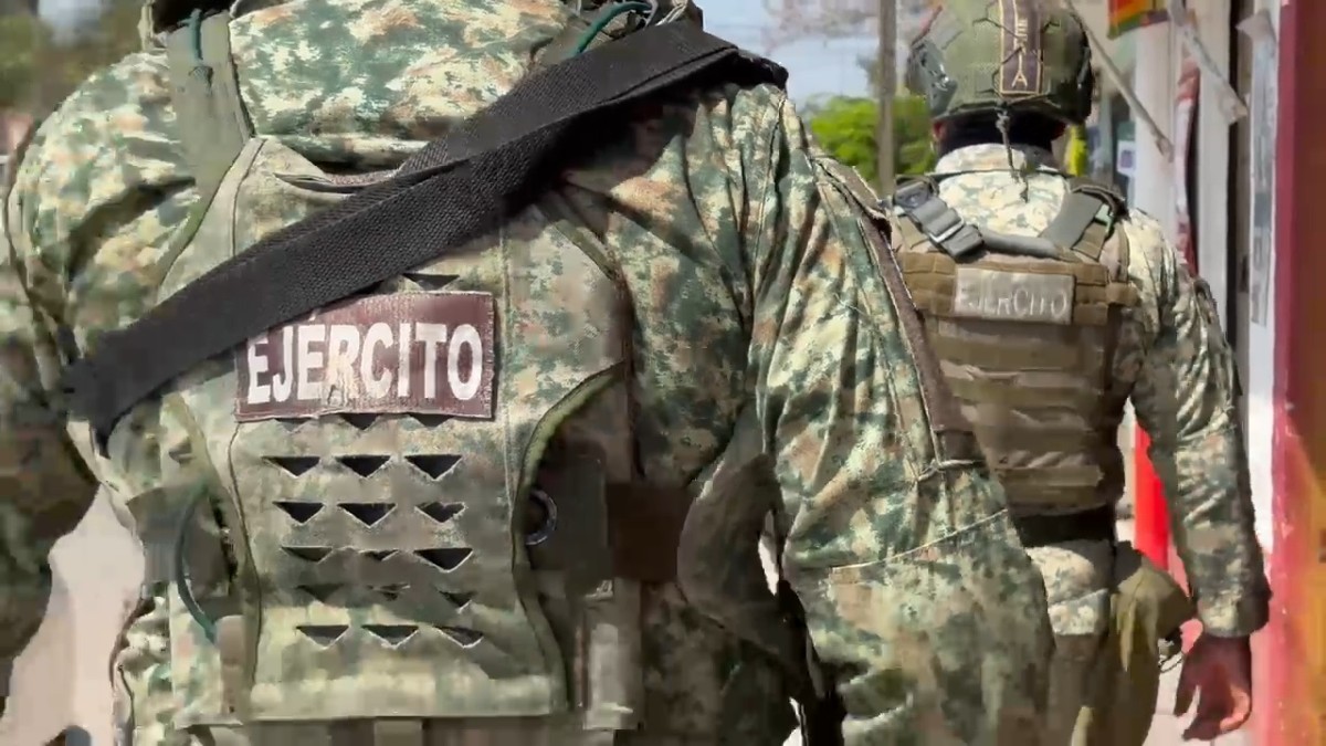 Dos militares del Ejército Mexicano vistos de espaldas mientras caminan por calles de El Salto al lado de una tienda de abarrotes