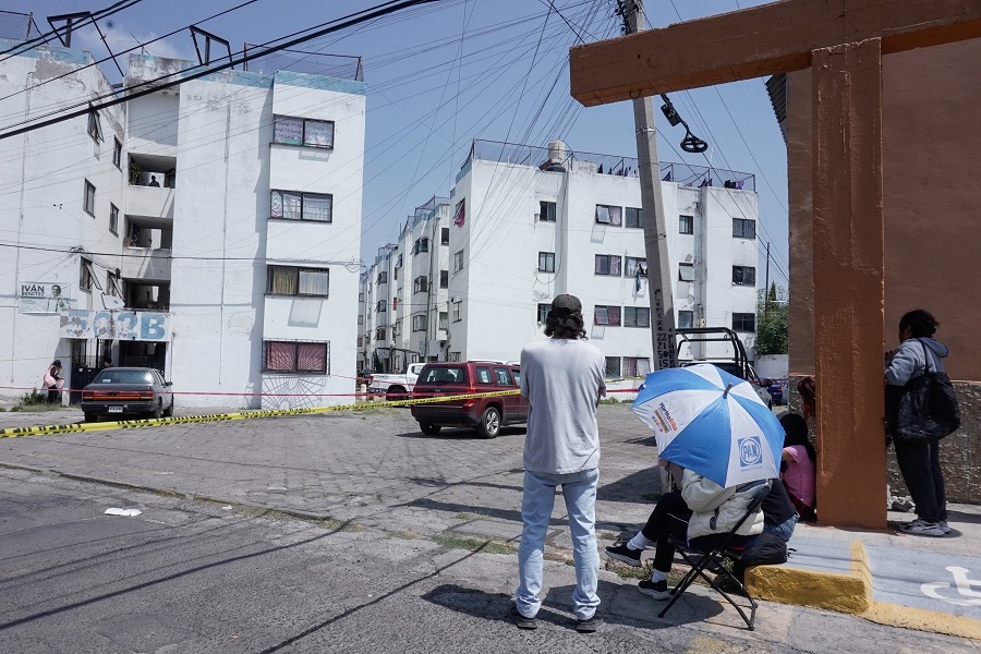 Personas observan detrás de una cinta de emergencia el cuerpo de un niño muerto tras caer de un edificio en Puebla.