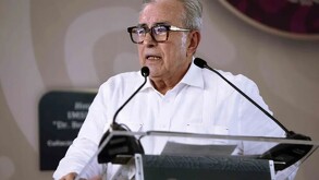 Rubén Rocha Moya, gobernador de Sinaloa, hablan frente al estrado con una camisa blanca y lentes cafés.